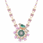 An ornate gold necklace featuring a bird pendant with a green emerald body, surrounded by pink gemstone flowers, white pearls, and sparkling clear stones, set against a plain white background.